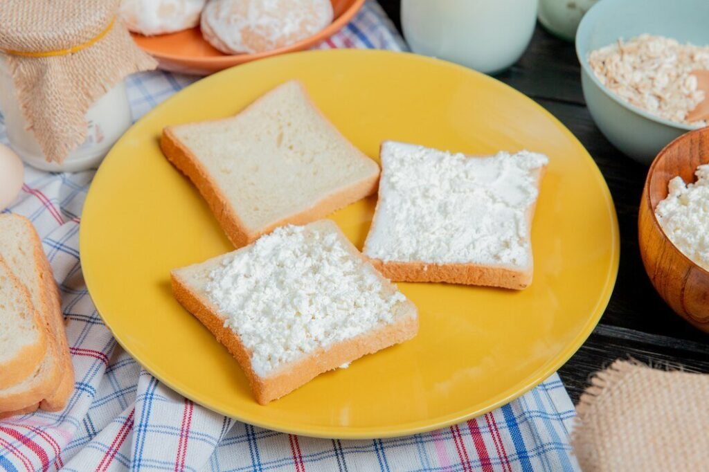 side-view-white-bread-slices-smeared-with-cottage-cheese-plate-with-gingerbreads-oat-flakes-cream-around-plaid-cloth-wooden-surface_141793-11421.jpg